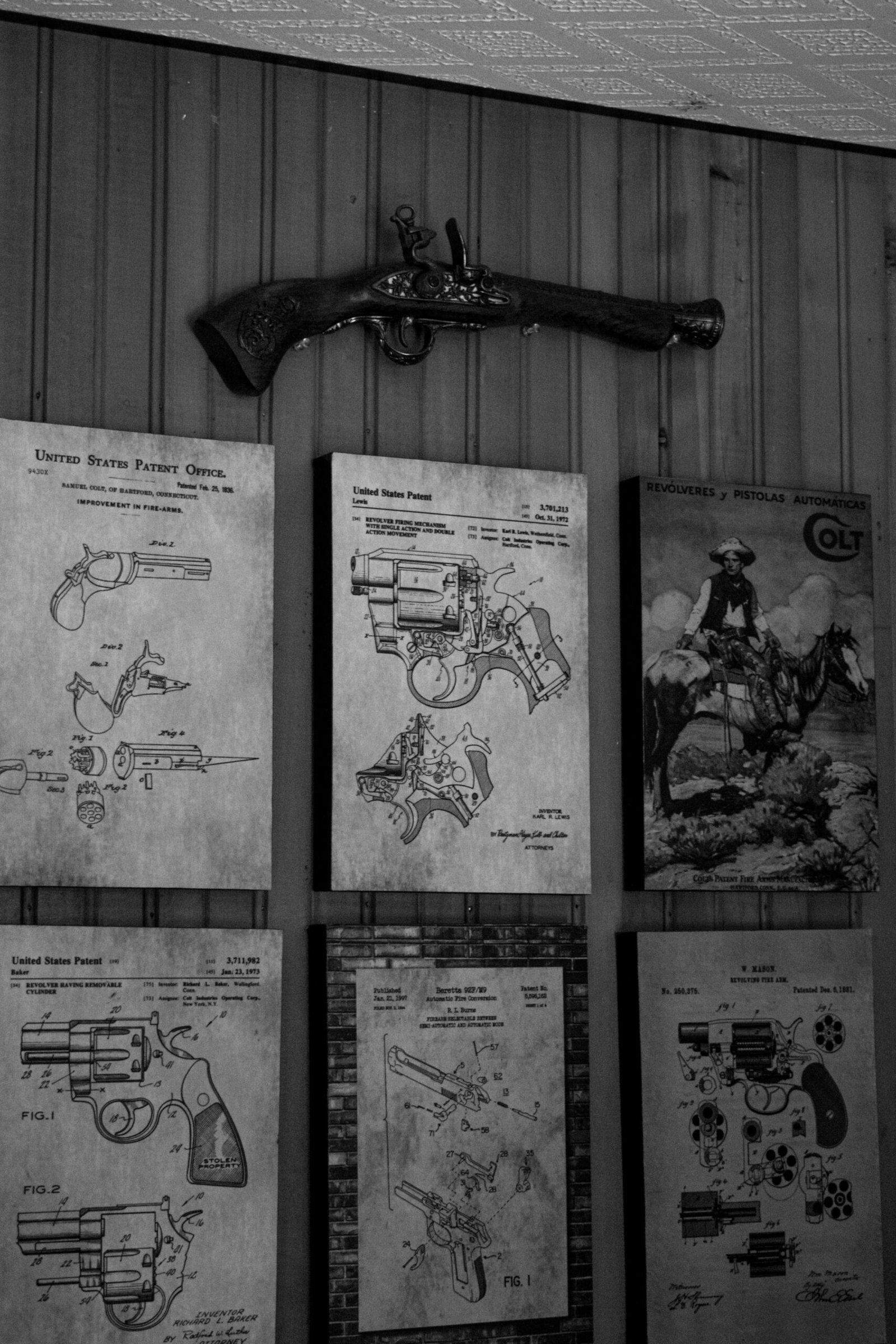 Black and white photo of historical gun blueprints and antique pistol on a wooden wall.